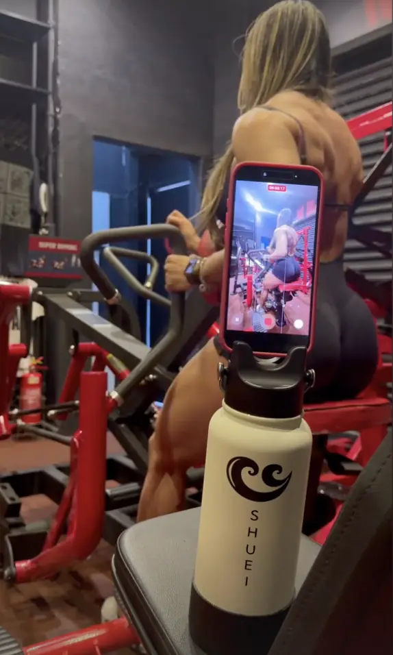 Cliente filma o treino de pernas com o celular na tampa-tripé da garrafa SHUEI creme